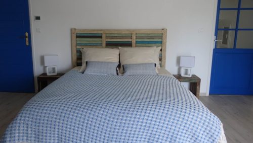 vue de la chambre Lapérouse, 1 grand lit, 1 tête de lit et 2 tables de chevet patinées dans différents coloris de bleu avec lampes de chevets blanches, 2 portes bleues.